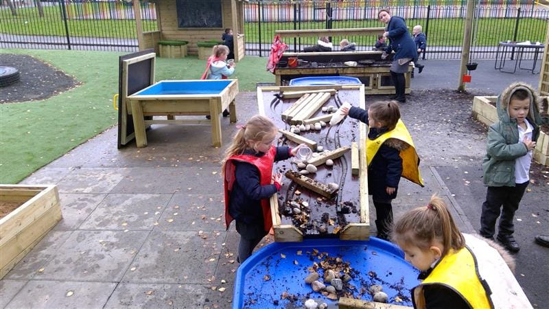 A class of children are playing with the water dam and have set up a variety of obstacles within the equipment to study the effects.