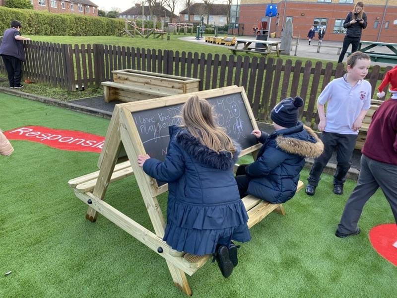 two pupils sit on the bench on the easel and draw on the chalkboard