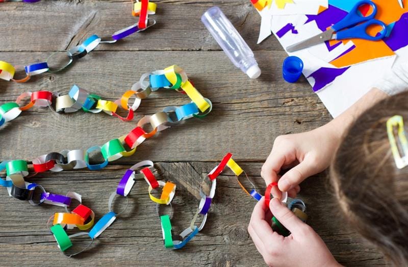 a zoomed in picture of a child's hands putting colourful paper chains together 