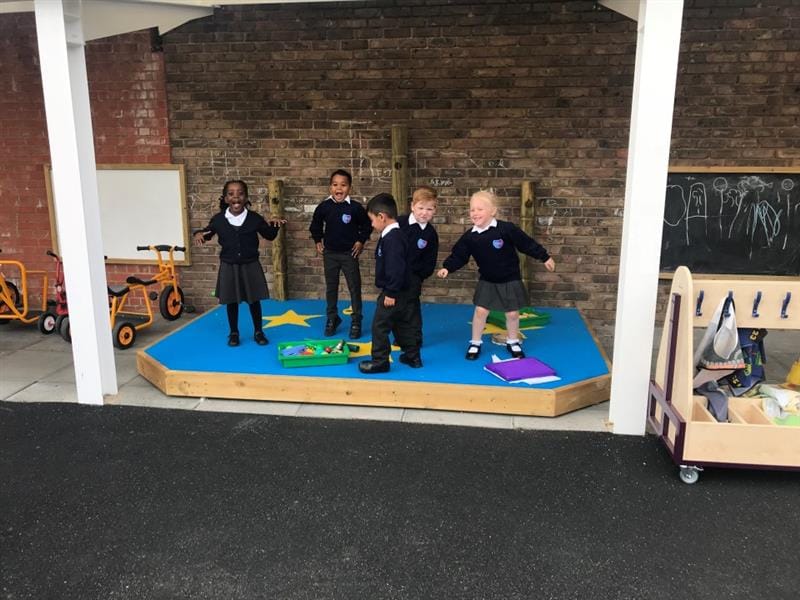 children in black school uniform dance around on a blue saferturf performance stage