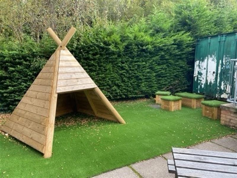 a wigwam sits on artificial grass with timber grass topped seats in the background