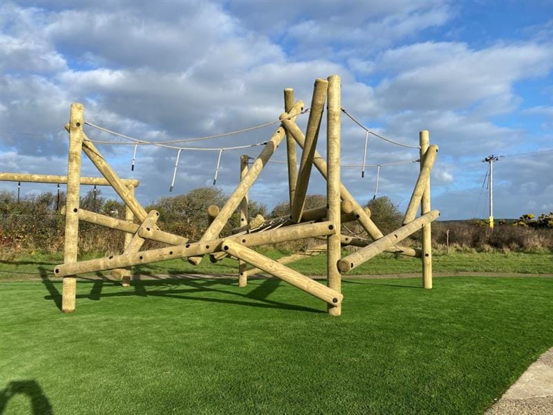 a timber climbing frame standing on artificial grass topped surfacing