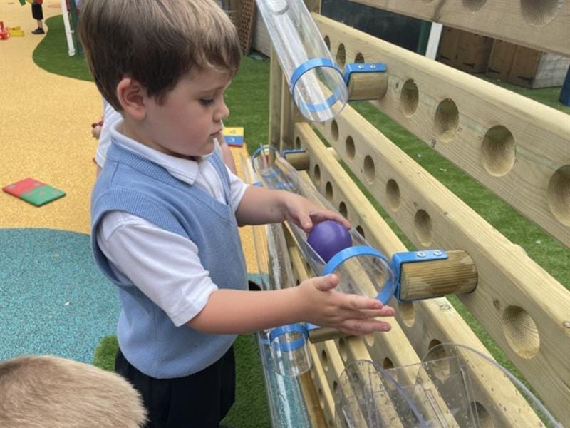a child stands close to the water wall and places a purple ball at the top of one pf the tubes pointing downwards