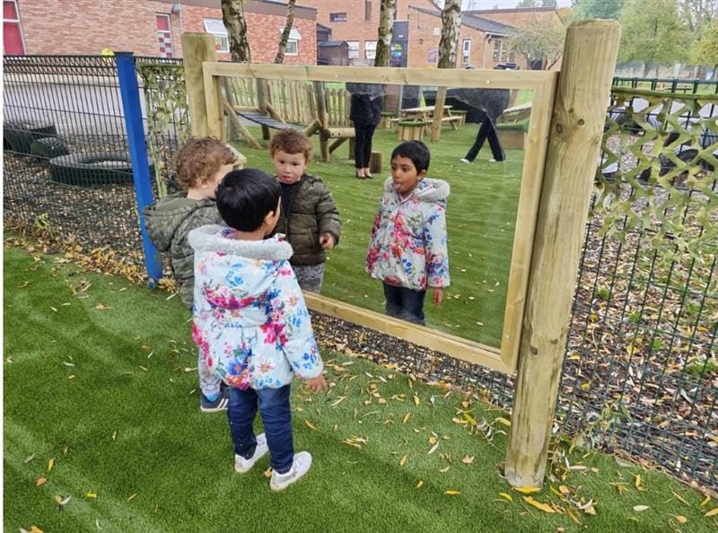 a little girl and a little boy look in the giant mirror at themselves whilst wearing winter coats