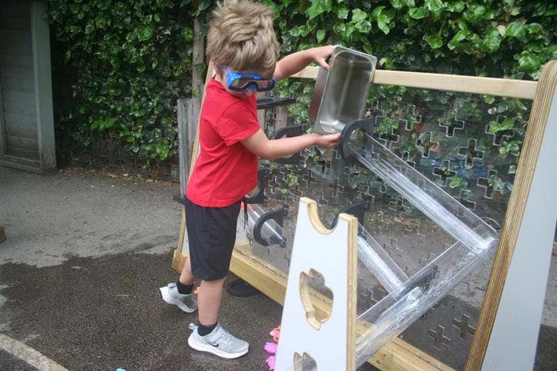 a child stands and pours water down the channels 