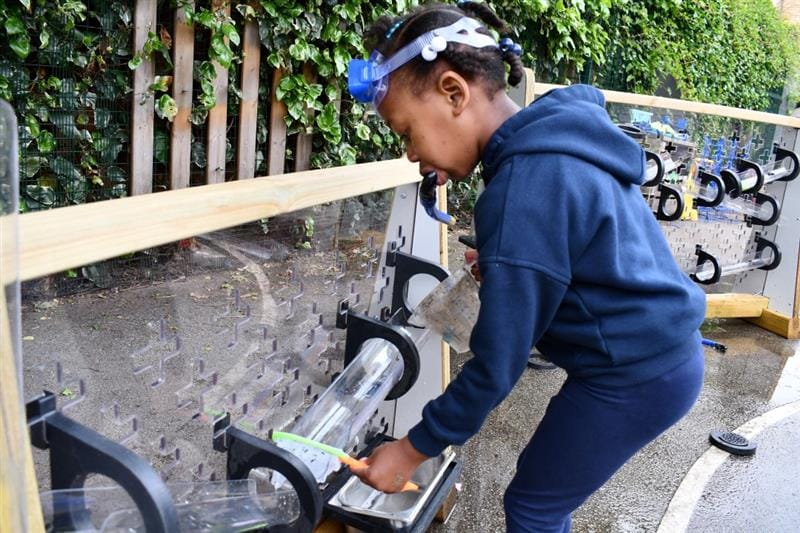 a little girl stands and pours water down the water wall