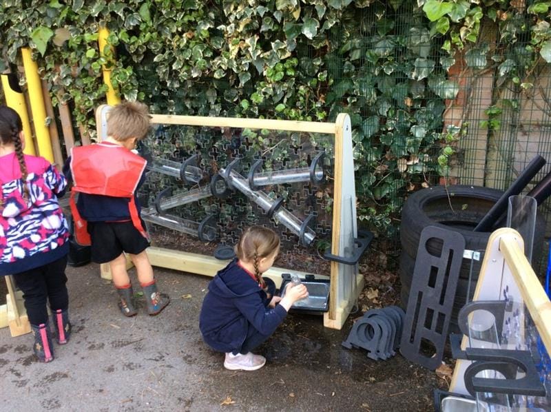 a little girl plays with the tray at th bottom of the new water wall whilst her classmates pour water down from the top