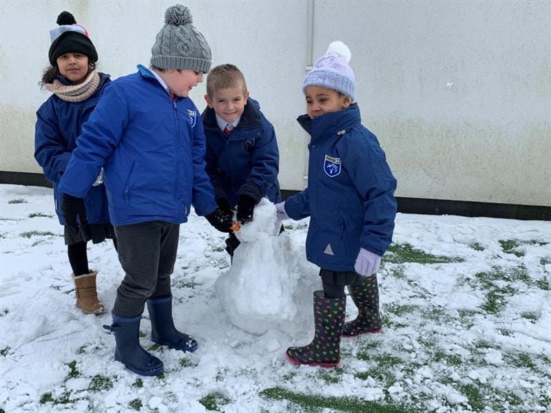 A group of children are building a snowman as they look at the camera.