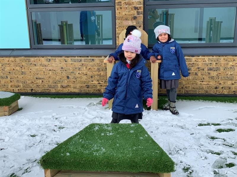 children stand and pose in front of the artifiical grass topped seats and storytelling chair