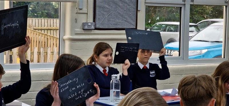 Two children sit at a table and hold their scribble boards up