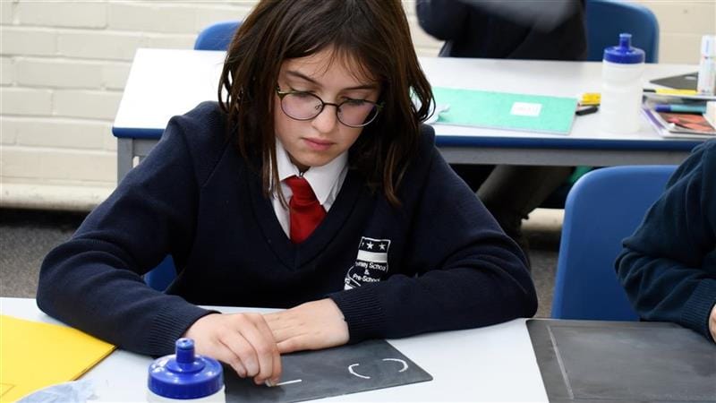 a little girl sits at a table and writes on the chalkboard with chalk