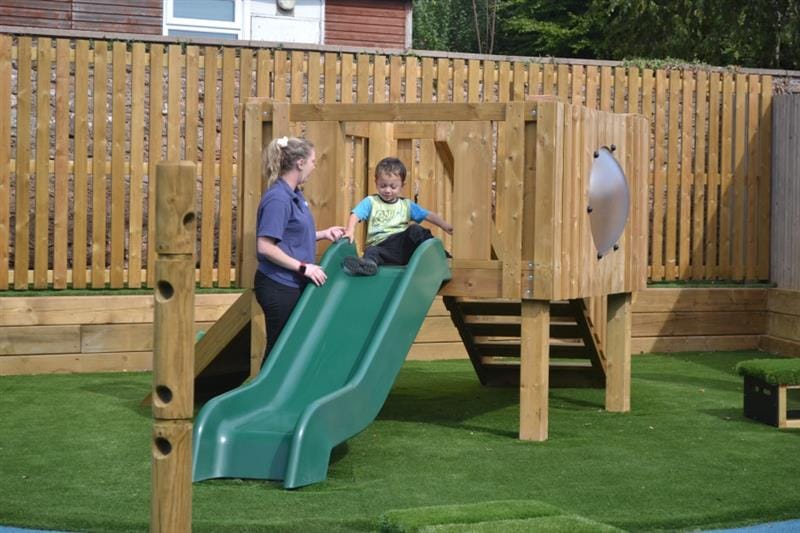 a child slides down the green slide on a low-level play tower