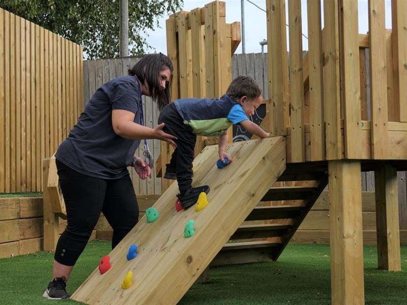 a child crawls up the rock climbing wall on the low level active play tower