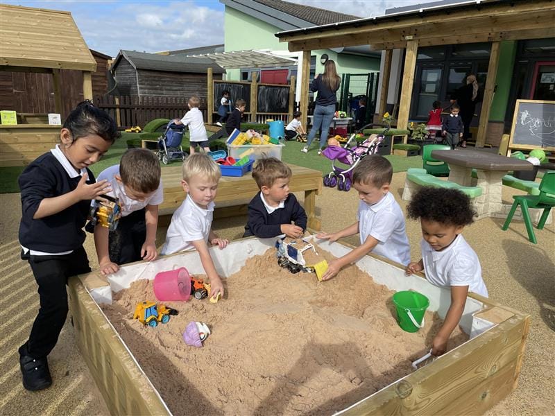 a low-level sandpit sitting on the floor with children gathering around playing with the sand