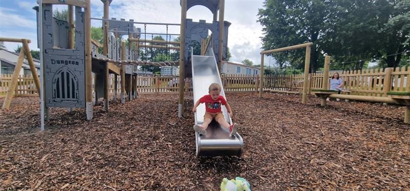 a little boy slides down the metal slide to the ground below