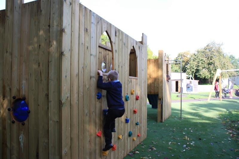 Child climbing up a vertical climbing wall on a playground castle as they pull themselves up using the multi coloured climbing holds