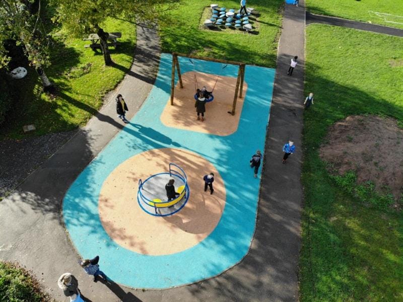 An overhead view of a kinetic play environment featuring a basket swing and a roundabout