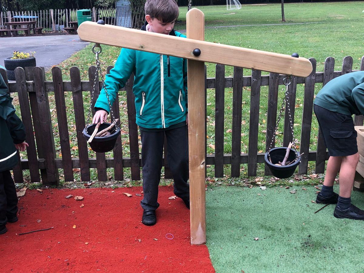 A boy is using a material weight scale to try and balance the scale by using different size sticks.