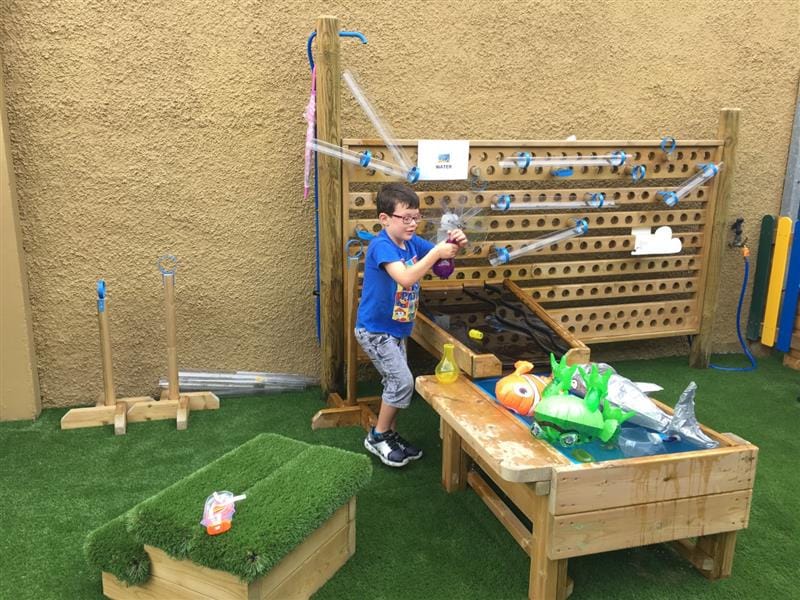 Child playing with a water wall and damming station with loose play resources
