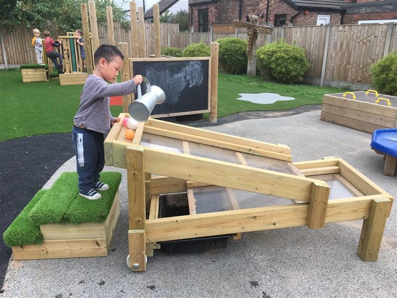 A boy at nursery is pouring water down the gravity table.