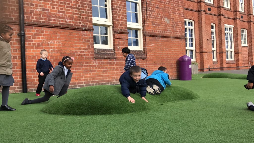 A small group of children are lying down on an artificial grass surface as they are all looking around in different directions.