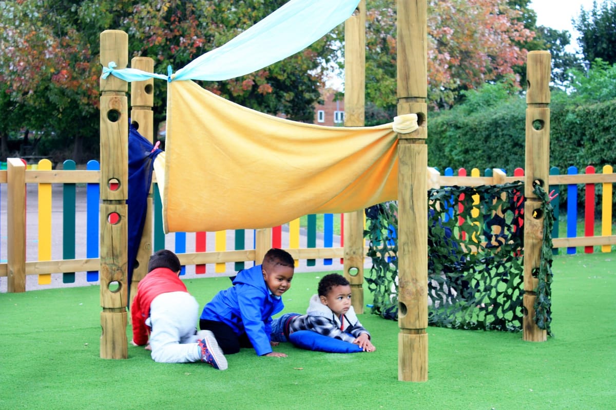 Three children are lay underneath a den that has been created from blankets being tied to 5 Den Making Posts