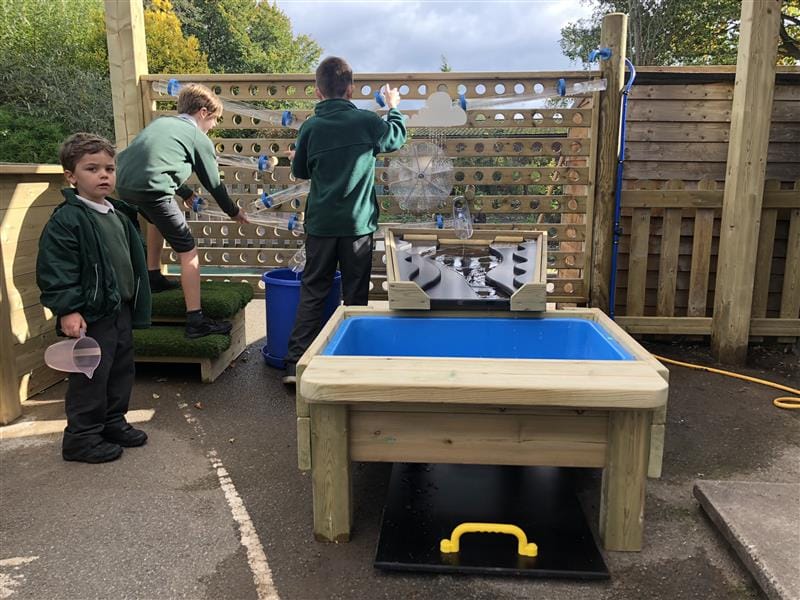 boys stand at the water wall and direct water down into the water table