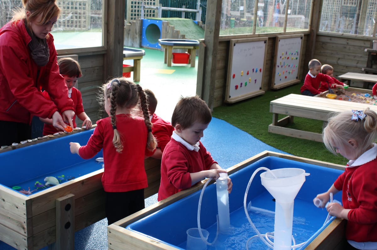 A group of children are using Water Tables to carry out experiments by using pipes and funnels to move water around in the tables.