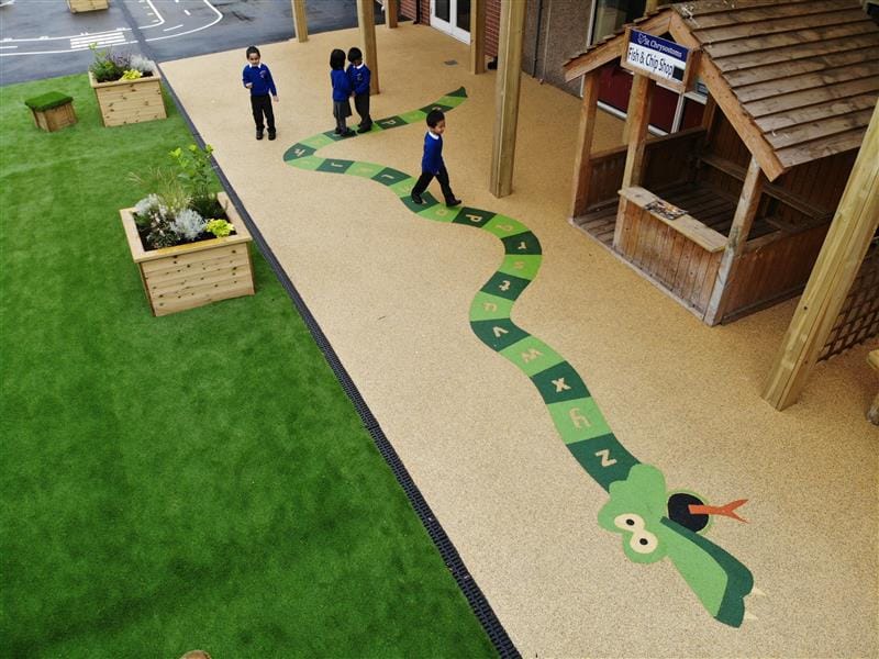 An overhead view of 4 children playing on a Alphabet Snake playground marking surrounded buy earth blend Wetpour