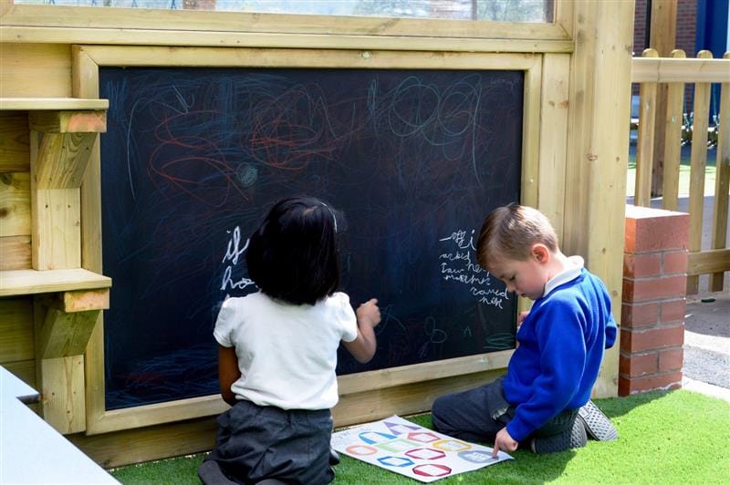 two children kneel on the floor in front of the chalkboard on posts and scribbles on it