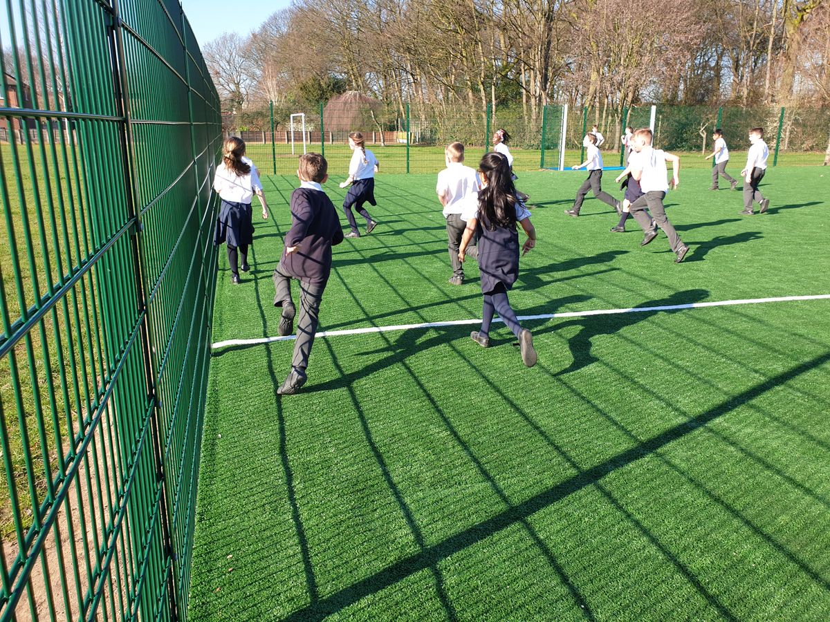 A large group of children are running around on a MUGA as they play a game of football.