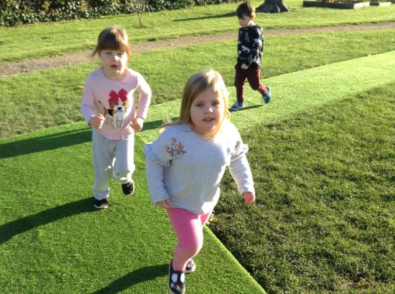 Three children are walking around a daily mile that has been installed in artificial grass.