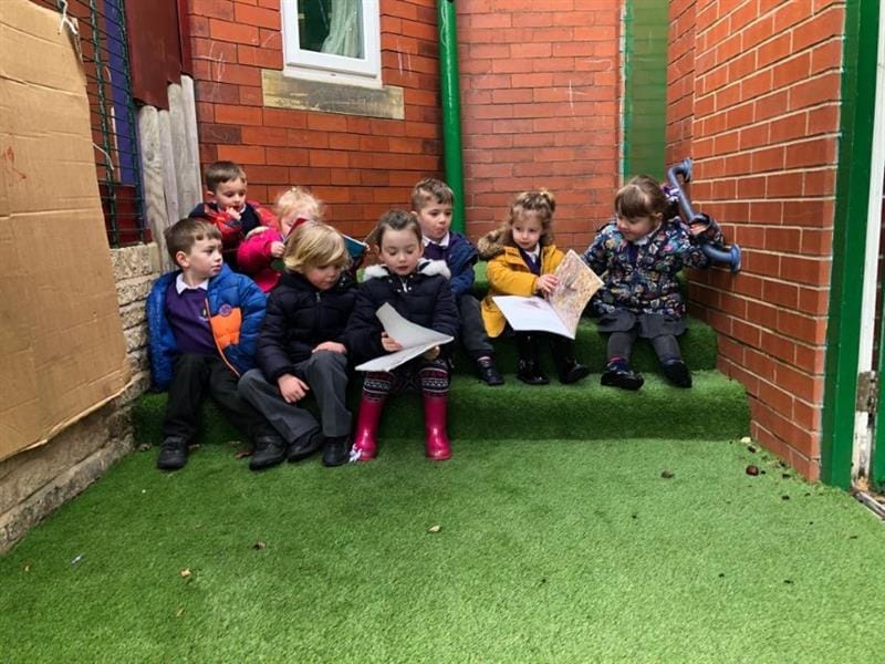 children sit on a grass topped step and read a book between them