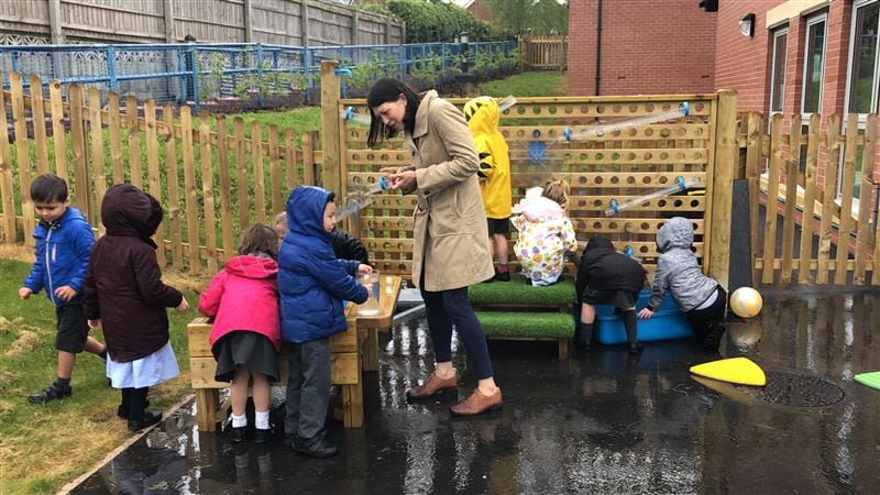 a teacher stands and helps the children as they play with the water wall