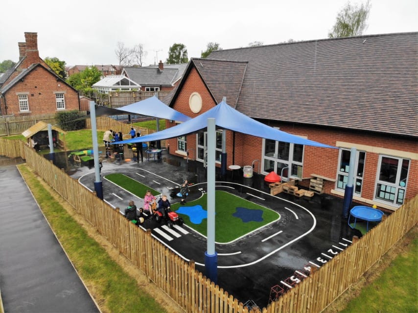 An EYFS play area that has a mixture of thermoplastic markings and artificial grass, all covered by two canopies.