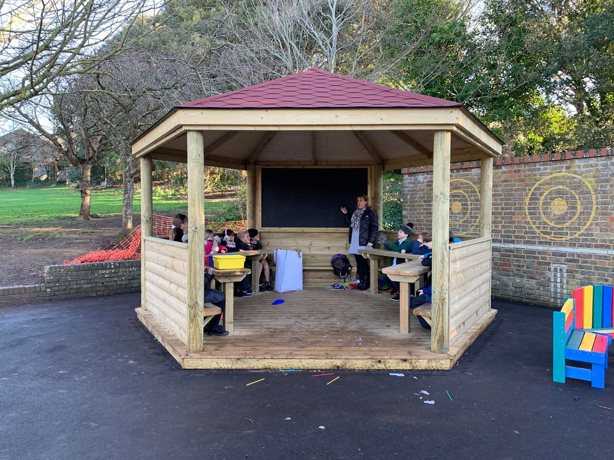 A teacher and her class are learning about phonics in an outdoor school canopy.