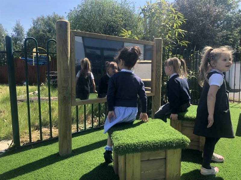 children sit on the grass topped seats and look in the mirror at themselves