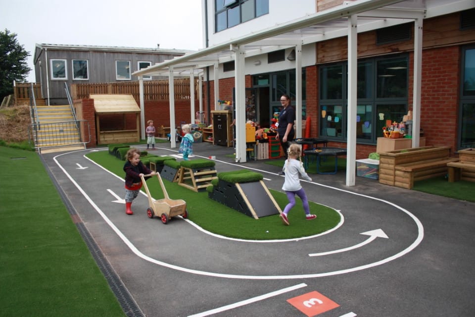 A playground which has thermoplastic markings in the design of a road. 4 children are running around and getting exercise