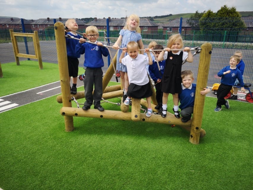 A group of children are playing on a climbing frame as they look at the camera and smile.