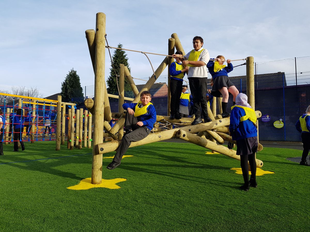 A group of primary school student are playing on a climbing frame as they look at the camera.