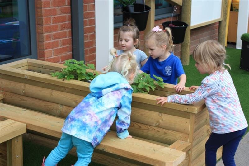 4 nursery children observing the plants in a planter bench and discussing their features
