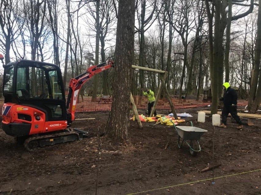 A team of installers are installing new play equipment in the middle of a forest.
