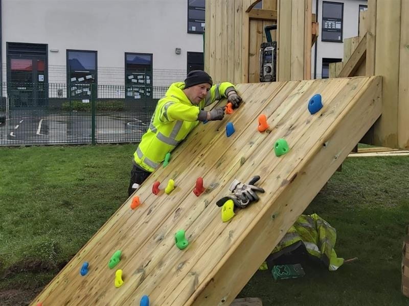 One of pentagon plays installers screwing in a handle to the climbing panel