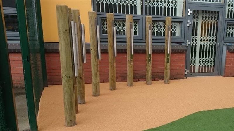 8 individual chimes are placed in a playground, showing the size of each pole and how they are accessible for children.