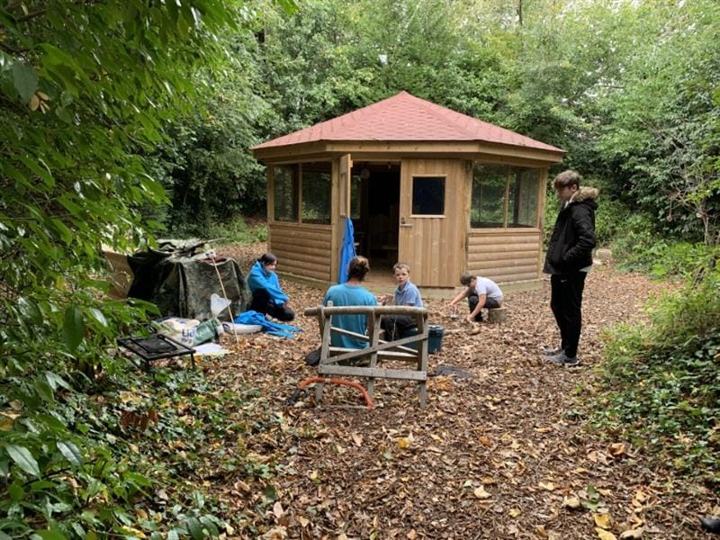 two children and three adults all playing in the outdoor classroom surrounded by forest.