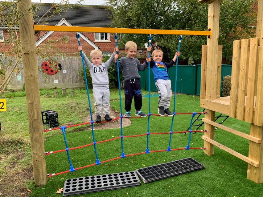3 children holding on to a climbing frame that has been designed and installed by Pentagon Play