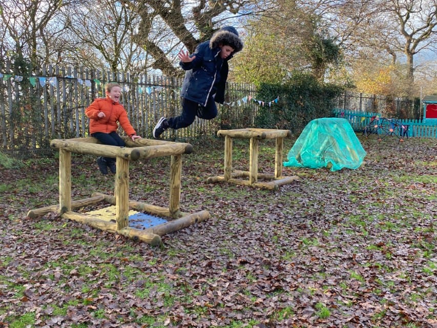 Two SEN boys are playing in nature and are jumping off play equipment.