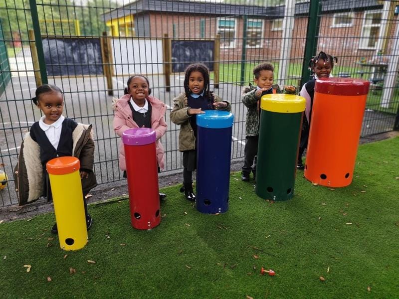 five children in winter coats and school uniform play with african drums as they smile at the camera