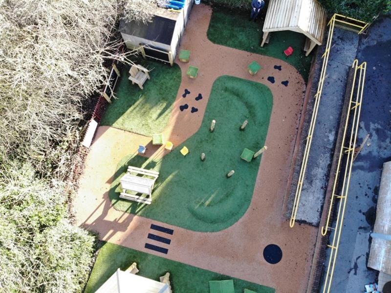 Aerial view of school playground which includes playground surfacing with a zebra crossing, artificial grass with 2 surfacing mounds and a giant playhouse. 