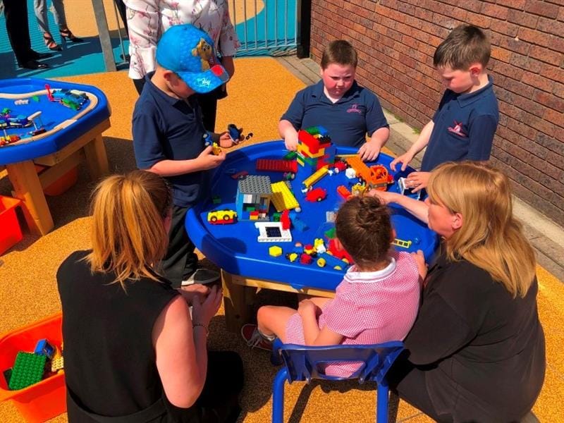 children sit around a tuff spot table with their teachers and play with construction toys